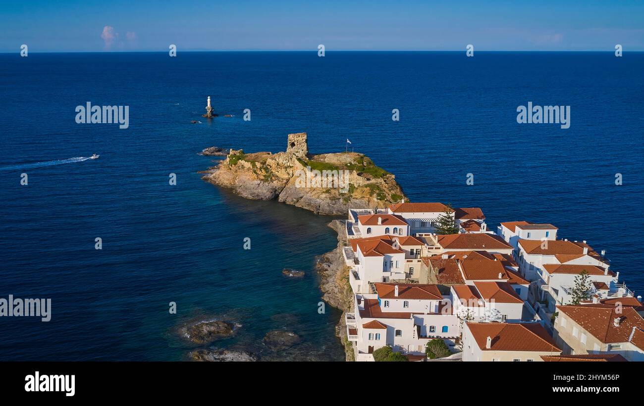 Drone shot, old town of Chora, houses with red tiled roofs, ruined fortress on offshore island, white round lighthouse on rock, boat moving from left Stock Photo