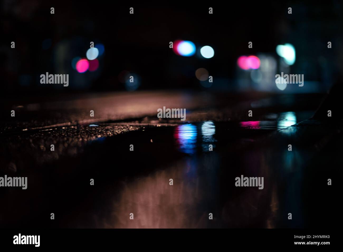 Closeup of a wet asphalt road reflecting bokeh blurry lights at night ...