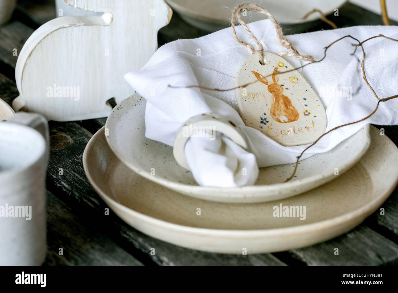 Rustic Easter table setting with empty craft ceramic tableware, plates and bowls, Easter bunny rabbit decorations, vase on wooden table. Easter holida Stock Photo