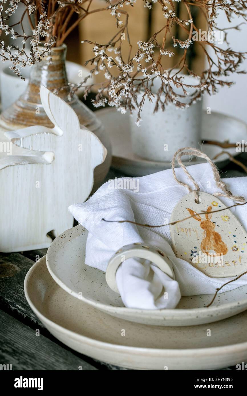 Rustic Easter table setting with empty craft ceramic tableware, plates and bowls, Easter bunny rabbit decorations, vase on wooden table. Easter holida Stock Photo