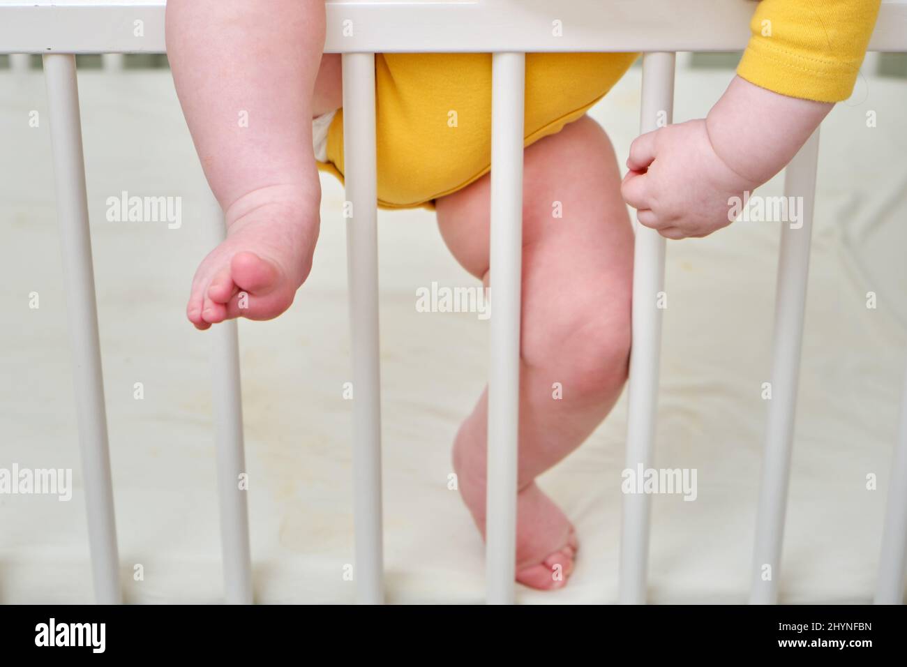 Toddler baby climbs the crib railing, legs closeup. Protect children