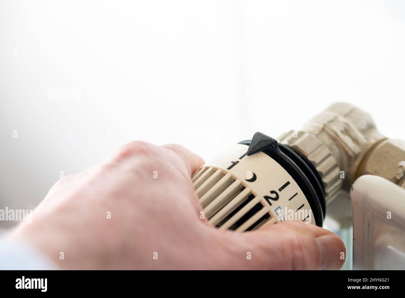 Close-up of hand turning thermostat down. Turn heating off. Gas price. Savings. Stock Photo