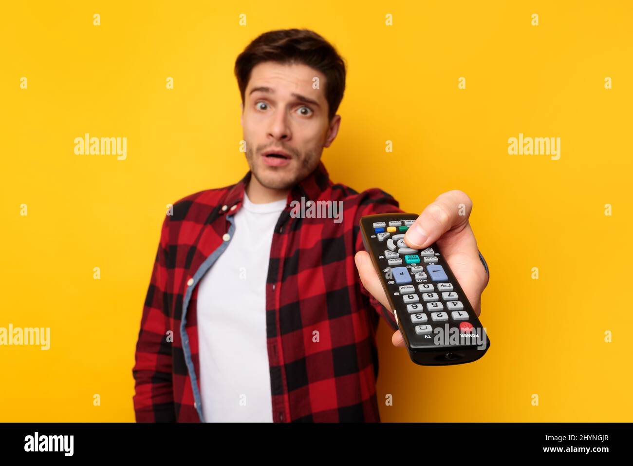 Scared young guy watching tv holding remote control Stock Photo