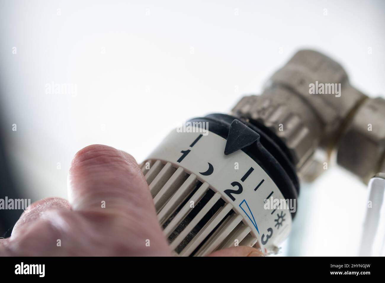 Close-up of hand turning thermostat down. Turn heating off. Gas price. Savings. Stock Photo