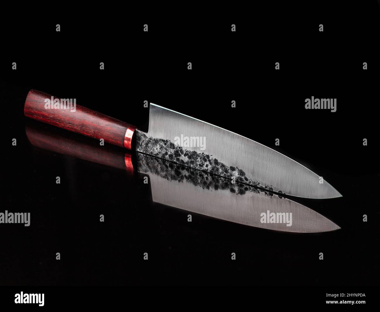 Sharp knife with a wooden handle and its reflection on a black surface
