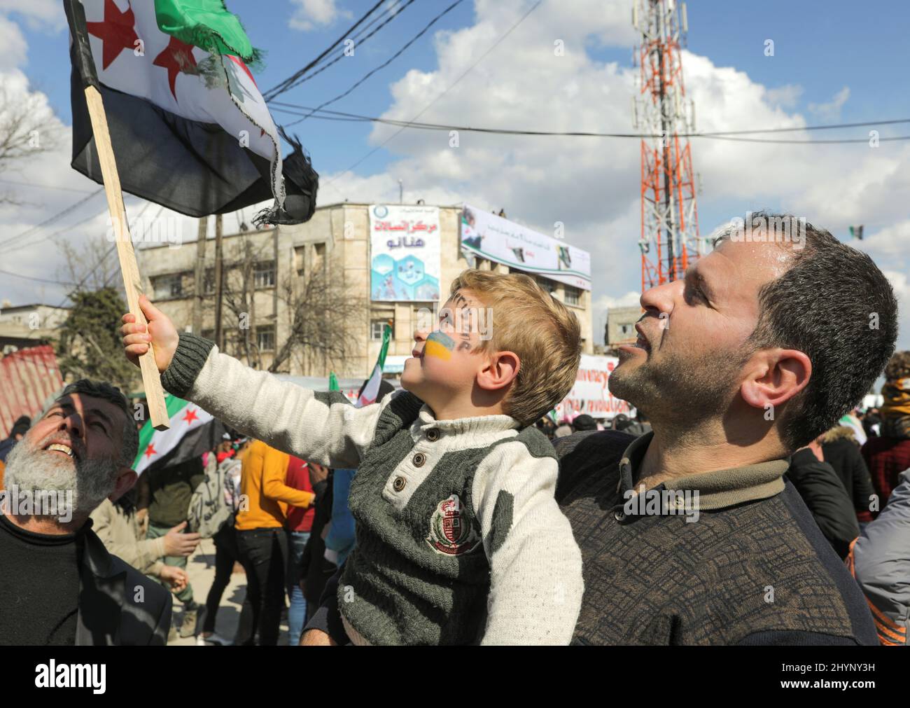 A boy holds an opposition flag with his face painted in colours of Ukrainian flag during a demonstration, marking the 11th anniversary of the start of the Syrian conflict, in the opposition-held Idlib, Syria March 15, 2022. REUTERS/Khalil Ashawi Stock Photo