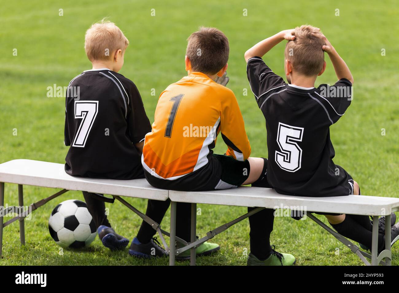 Soccer players sitting on sideline bench. School football team. Youth soccer players sitting together on substitute bench and watching match Stock Photo