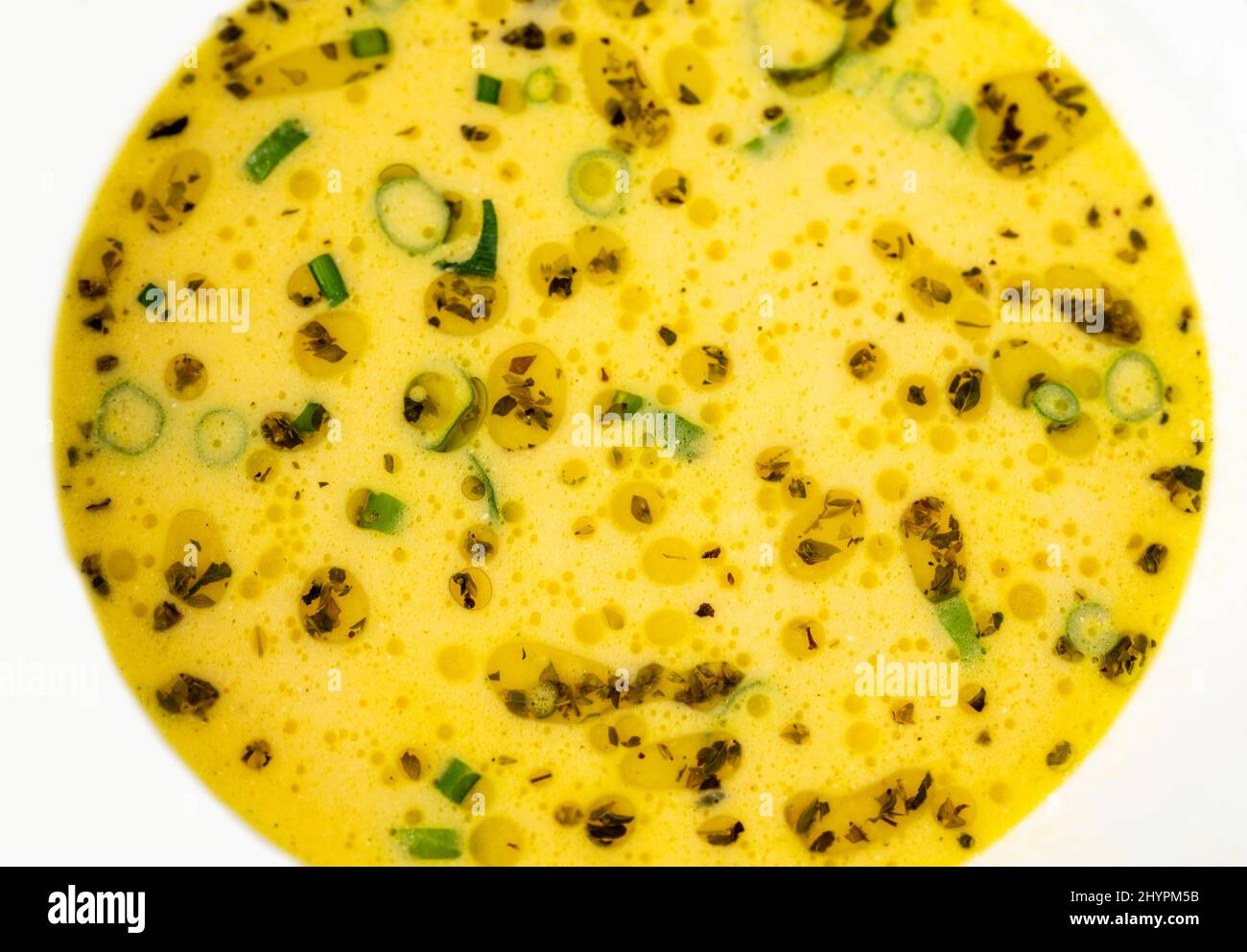 Cheese soup, detail of yellow decorative surface with oregano herb, green onion shoot and oil circle in white plate. Stock Photo
