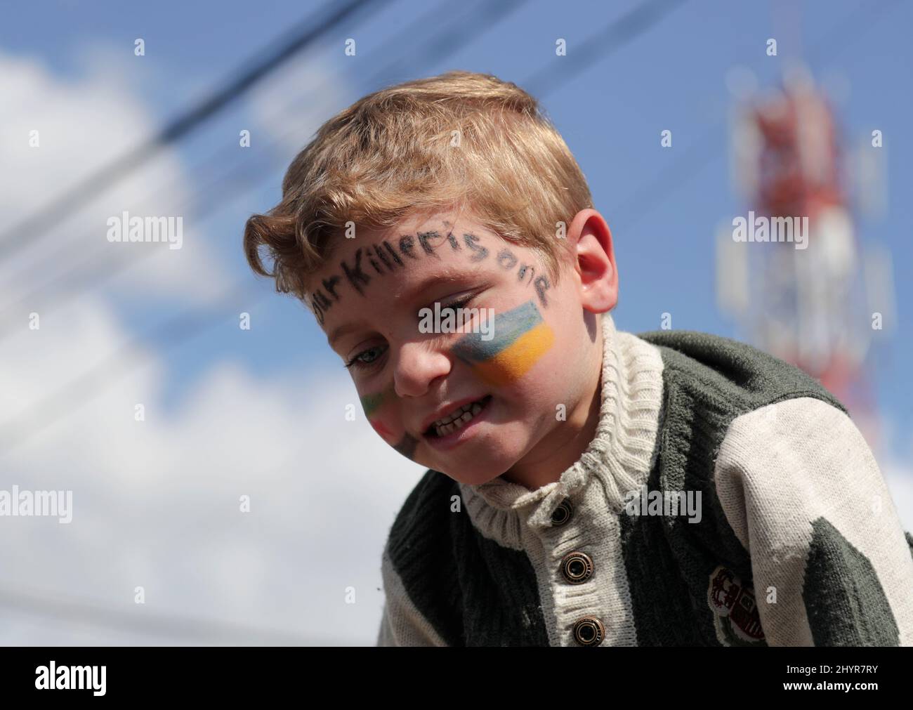 A boy with his face painted in colours of Ukrainian flag takes part in a protest marking the 11th anniversary of the start of the Syrian conflict, in the opposition-held Idlib, Syria March 15, 2022. REUTERS/Khalil Ashawi Stock Photo