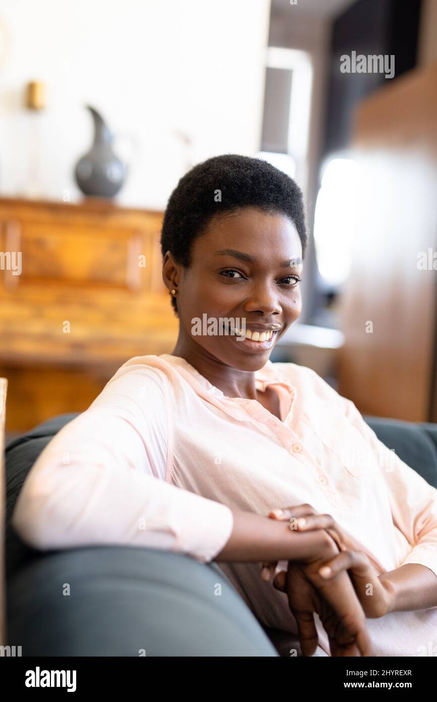 Portrait of happy african american young woman sitting on sofa in ...