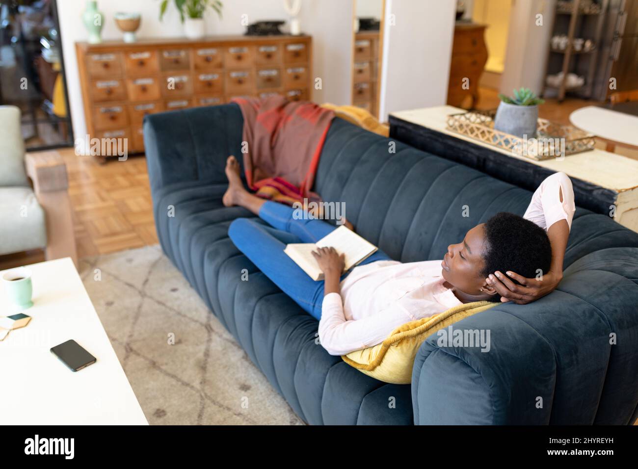 Relaxed african american woman lying on sofa with book in living room ...