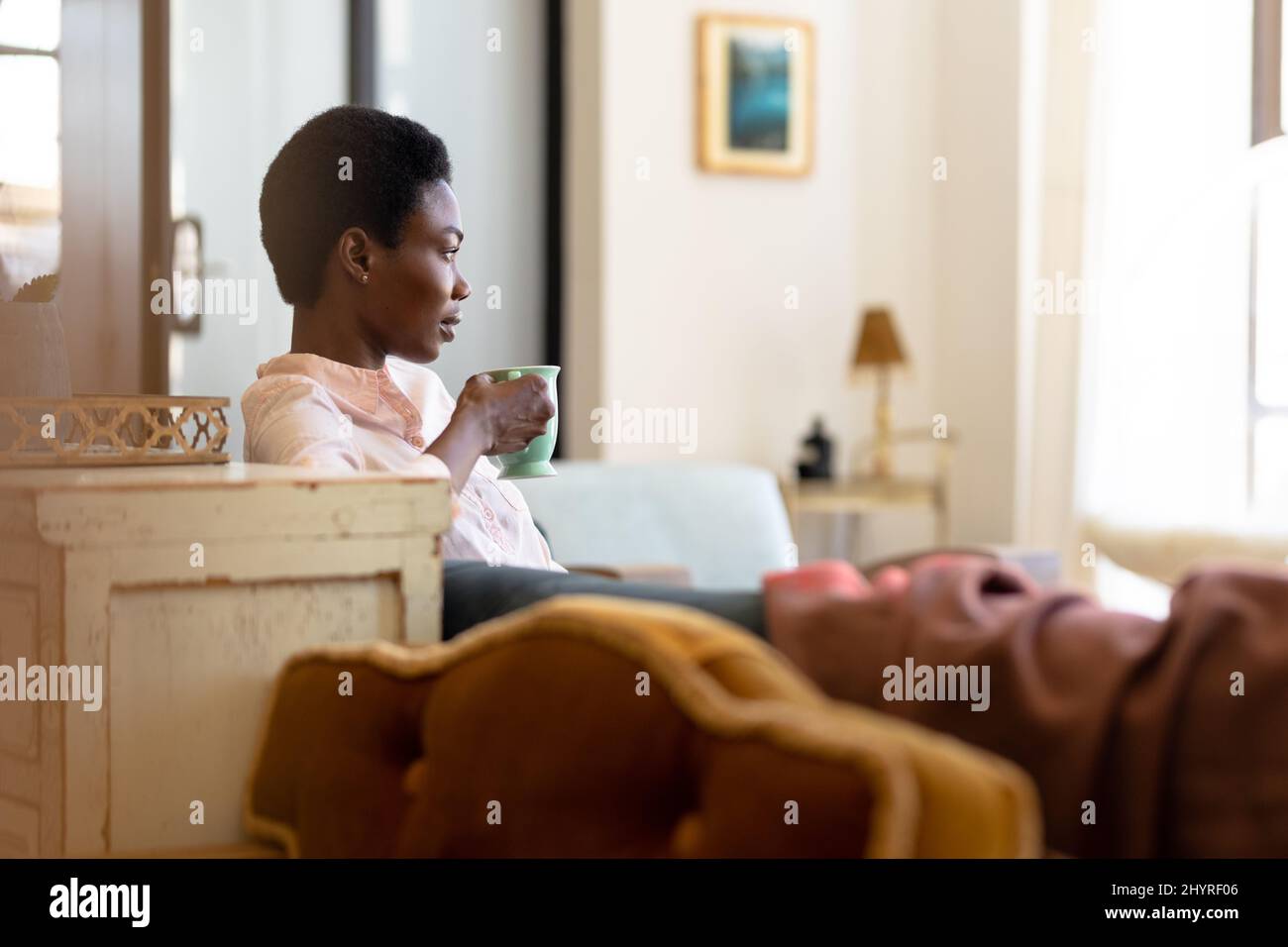 Thoughtful african american woman sitting on sofa with coffee mug ...