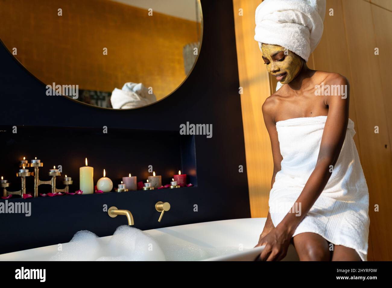 African american young woman wearing towel sitting on bath tub in bathroom at home Stock Photo ...