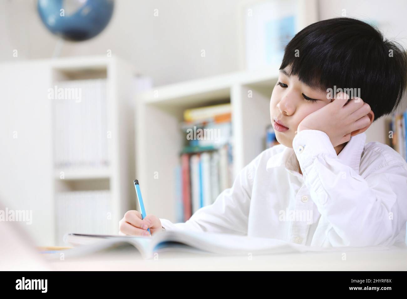A student exhausted from the piled up of school homework and tedious study is learning by solving difficult problems with a tired look. Stock Photo