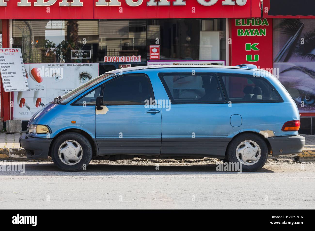 Side, Turkey -February  18, 2022: blue Toyota Previa   is parked  on the street on a warm day against the backdrop of a buildung,   park, fence, shops Stock Photo
