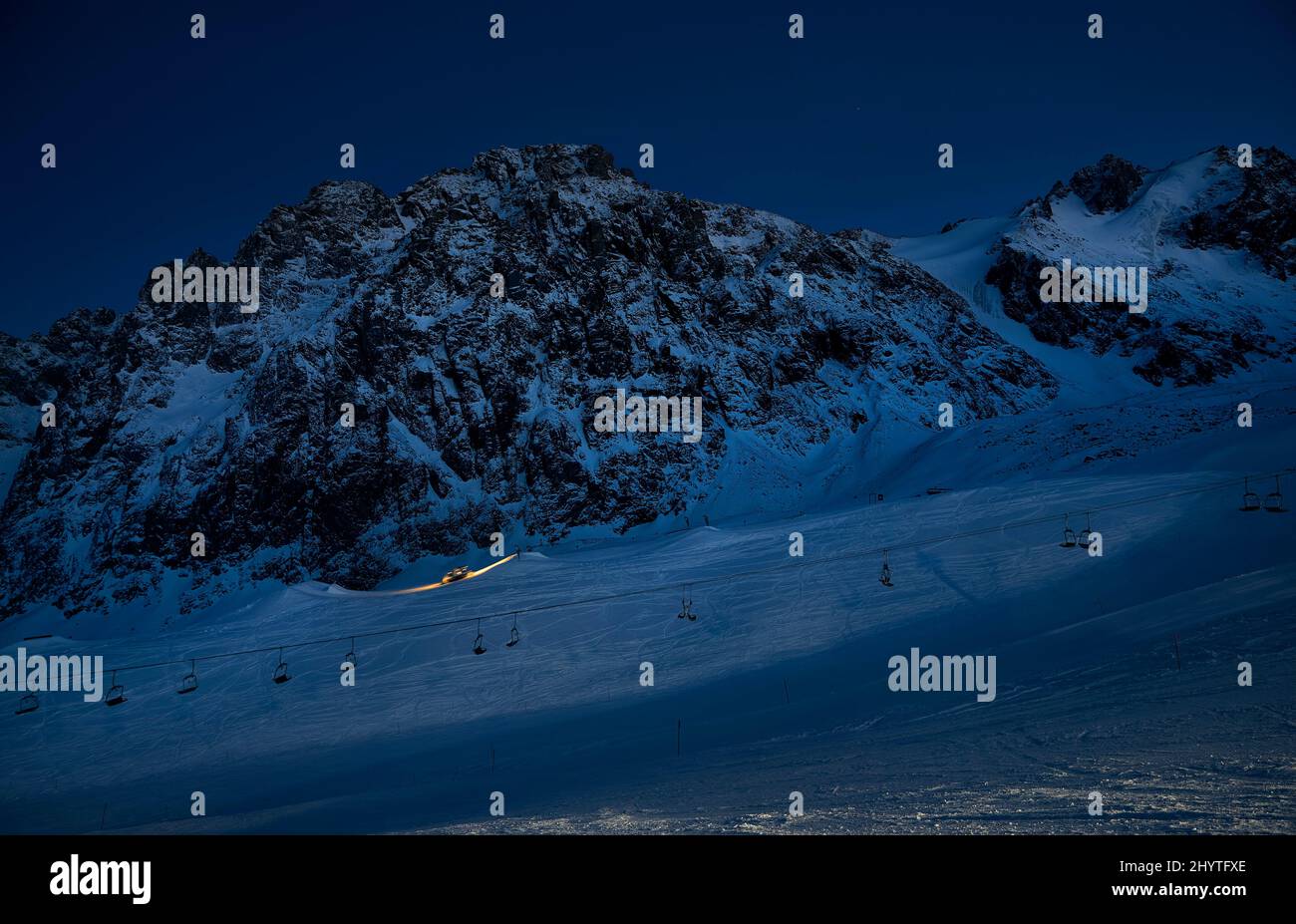 Silhouette of modern snowcat ratrack with led light preparing ski slope at night snow park with star sky at Shymbulak ski resort Almaty, Kazakhstan Stock Photo
