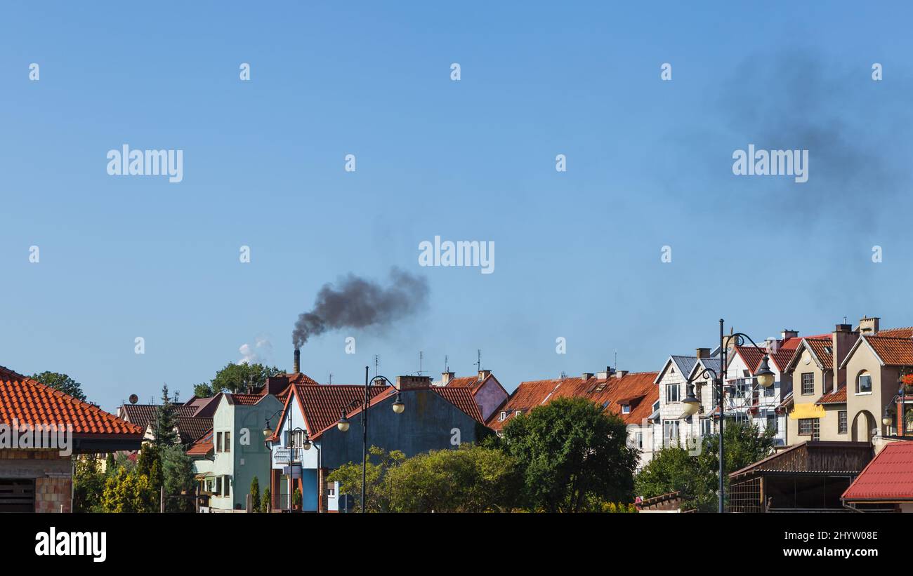 Air pollution, black smoke from chimney over urban area, small one family houses in the city against blue sky with copy space Stock Photo