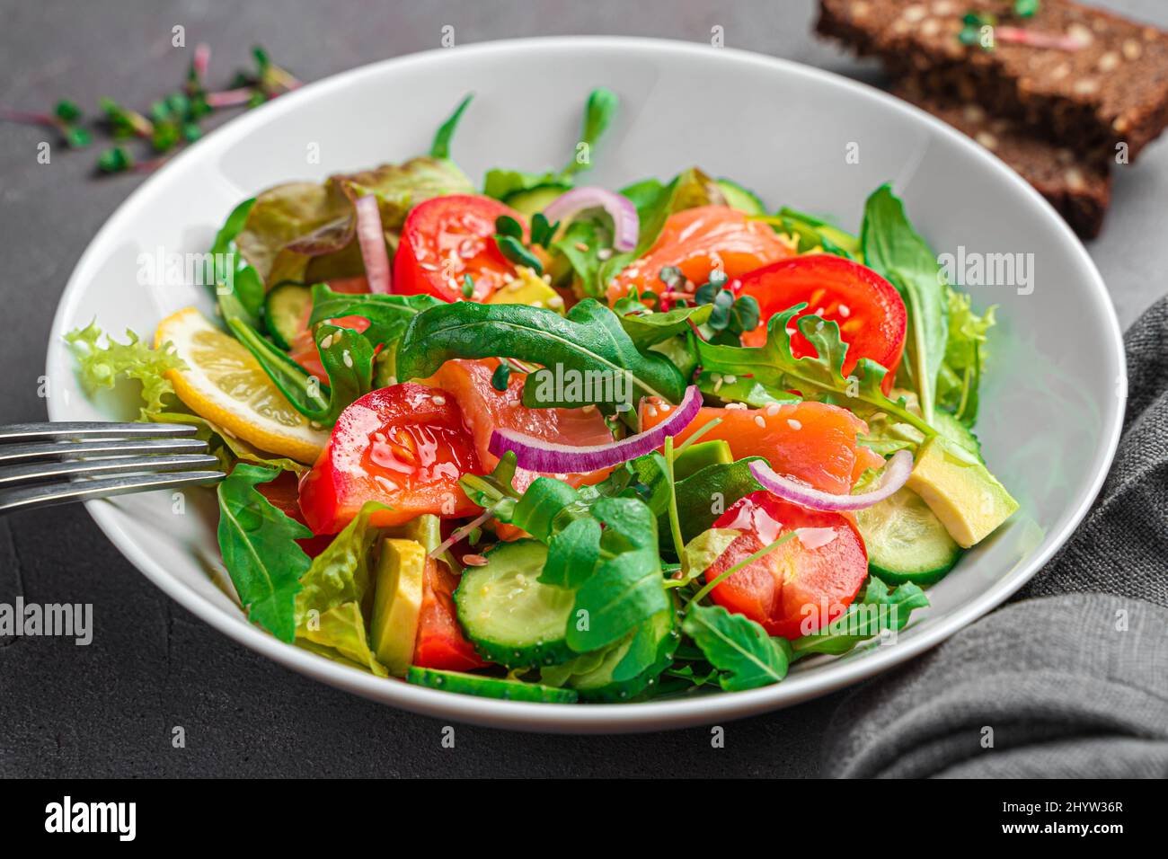 Vegetable salad with salmon and fresh herbs on a dark background. Side view, close-up. Stock Photo