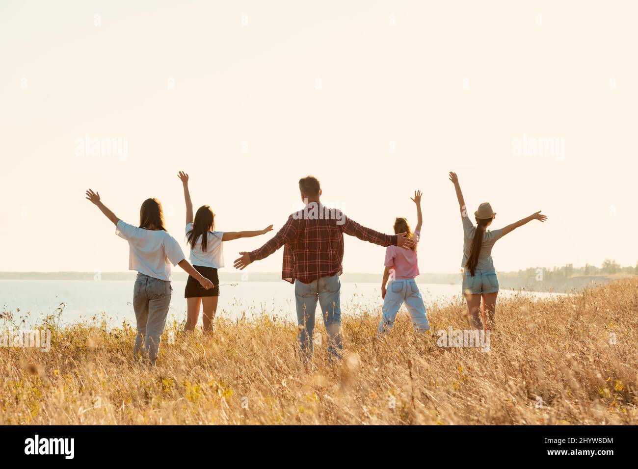 Group of happy friends stands with raised arms at sunset Stock Photo