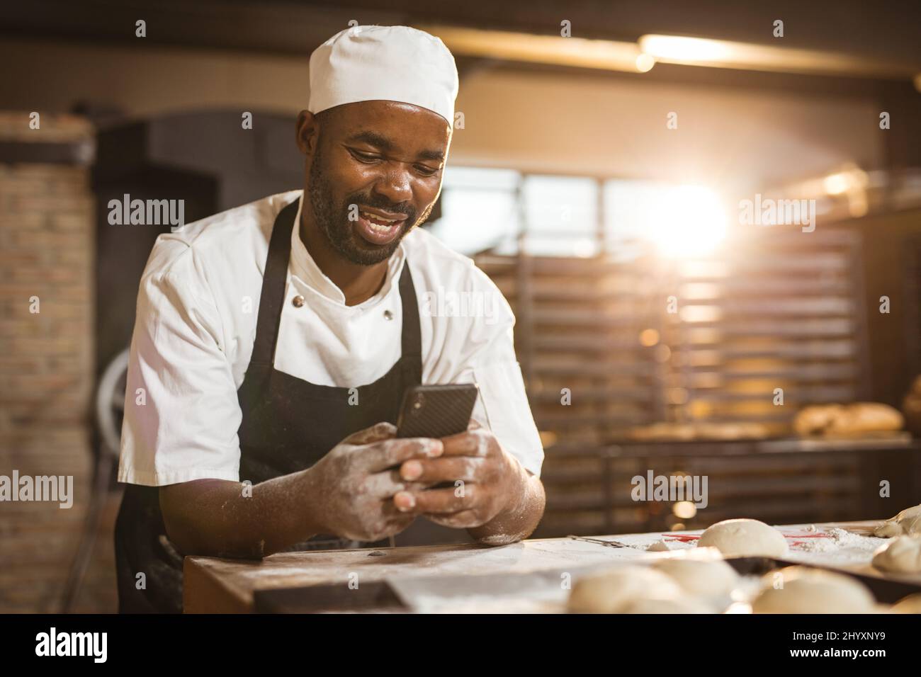 Smiling african american mid adult male baker using smart phone while