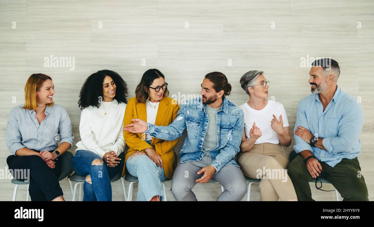 Happy businesspeople talking to each other while sitting in line for an interview. Group of successful job applicants getting to know each other in a Stock Photo