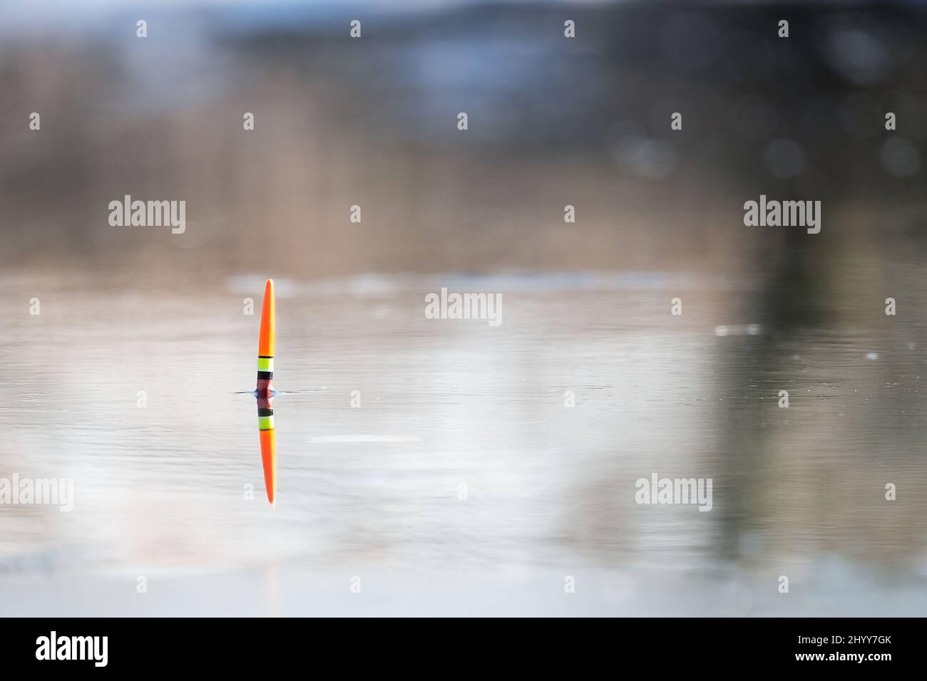 Orange-yellow fishing float in the river water. Spring fishing, bright colors of water and nature. Solar reflection in the water. Background image. Stock Photo