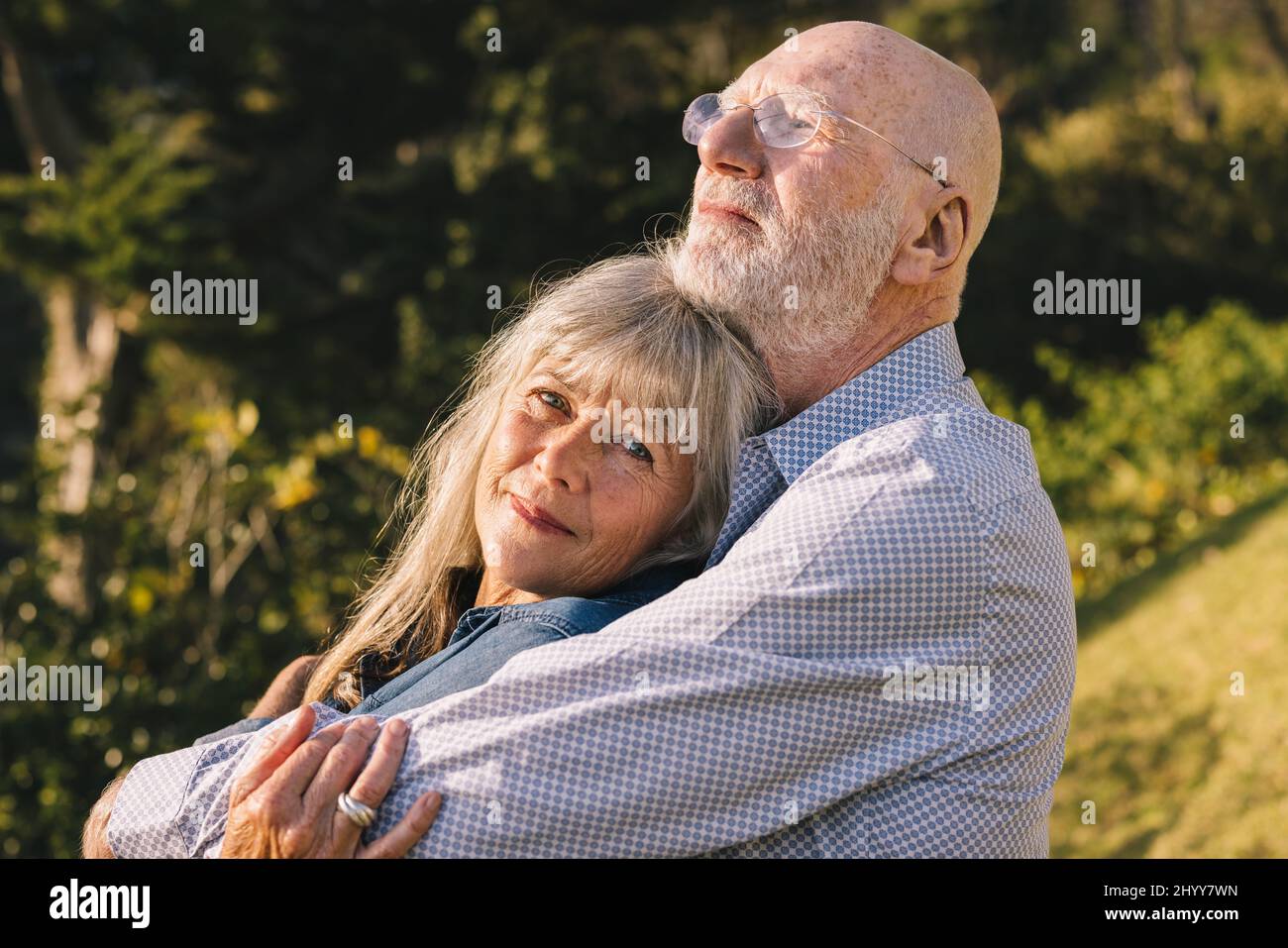Senior couple embracing each other while standing in a park. Romantic elderly couple enjoying the sun in each other's arms. Mature couple spending qua Stock Photo