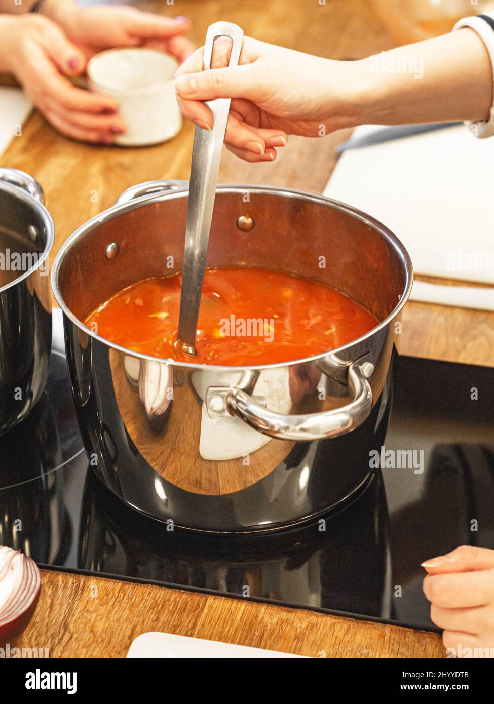 Uncertain woman preparing soup in the kitchen at home. A woman stirs tomato soup in a saucepan on the stove with a spoon. Stock Photo