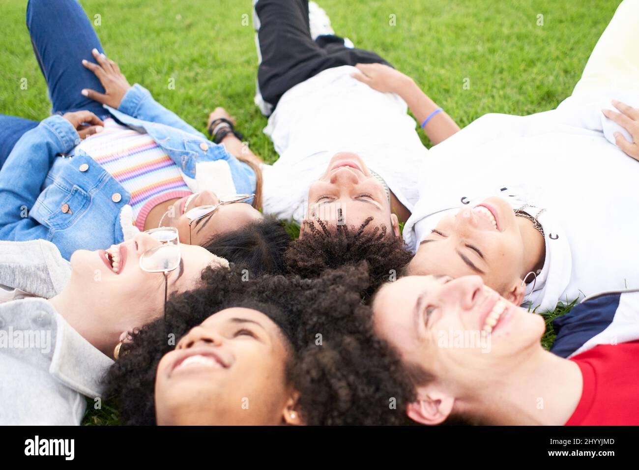 Group of happy teenagers friends having fun together outdoors. Smiling multiracial young people enjoying lying on the grass in the park. Stock Photo