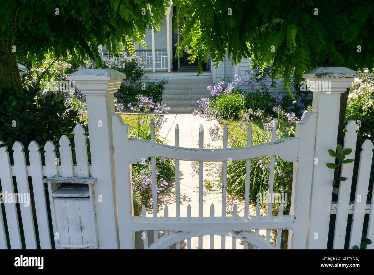 Closed gate leading to path through grounds and flowers to residence Stock Photo