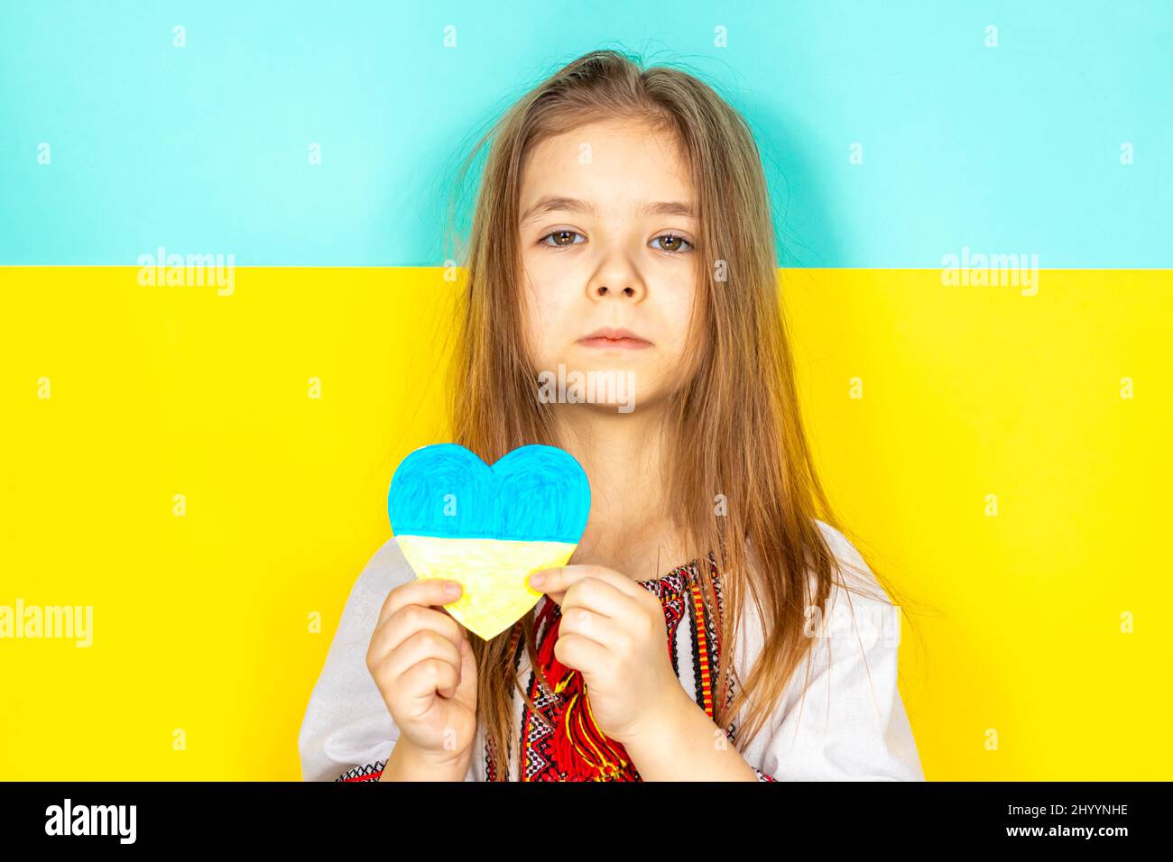 A girl in a national Ukrainian vyshyvanka holds a heart painted in yellow and blue tones as a sign of love for Ukraine, close-up against the Stock Photo