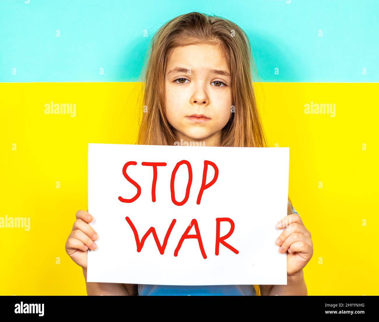 A girl is crying, holding a STOP WAR poster in her hands against the background of the Ukrainian flag. Stop the war in Ukraine. The concept of peace Stock Photo