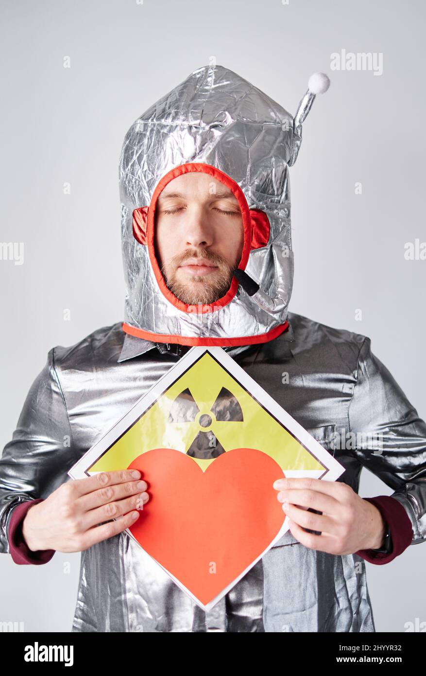 Young bearded caucasian astronaut man or nuclear power plant worker standing by the wall. Male in spacesuit with red paper heart. Romance, relationships concept. High quality image Stock Photo