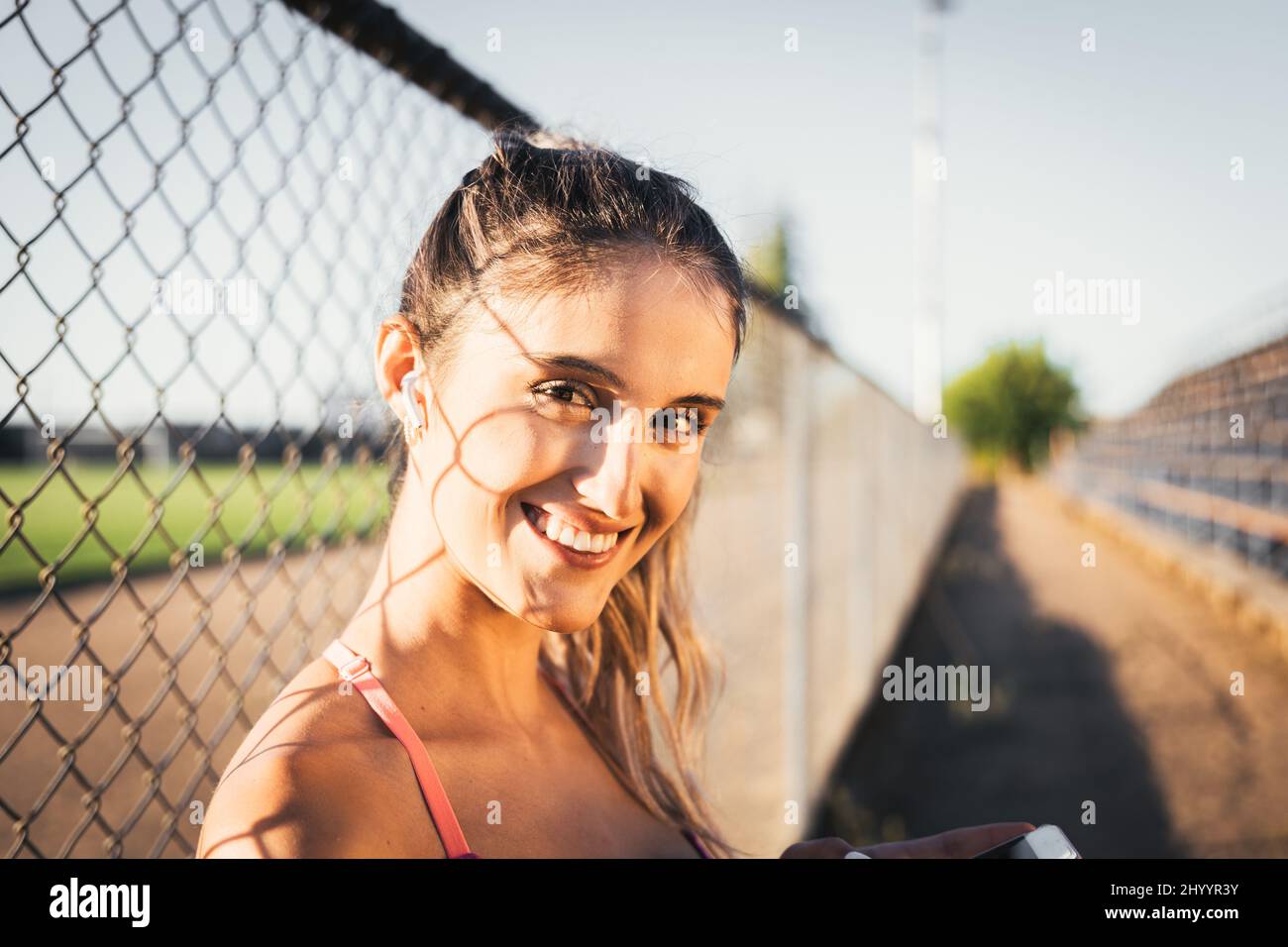 Smiling caucasian young active woman looking at the camera and setting a music playlist on her smartphone  Stock Photo