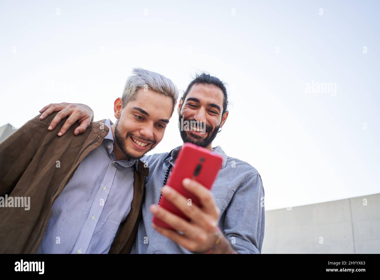 Homosexual man couple together using phones. Happy gay people watching something at mobile cell. Stock Photo