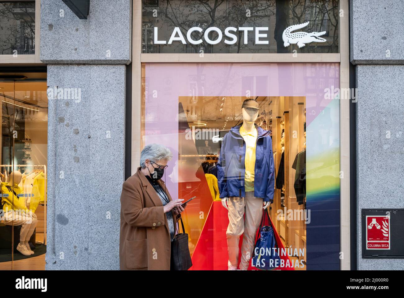 A pedestrian walks past the French clothing brand Lacoste store and logo in Spain Stock Photo Alamy
