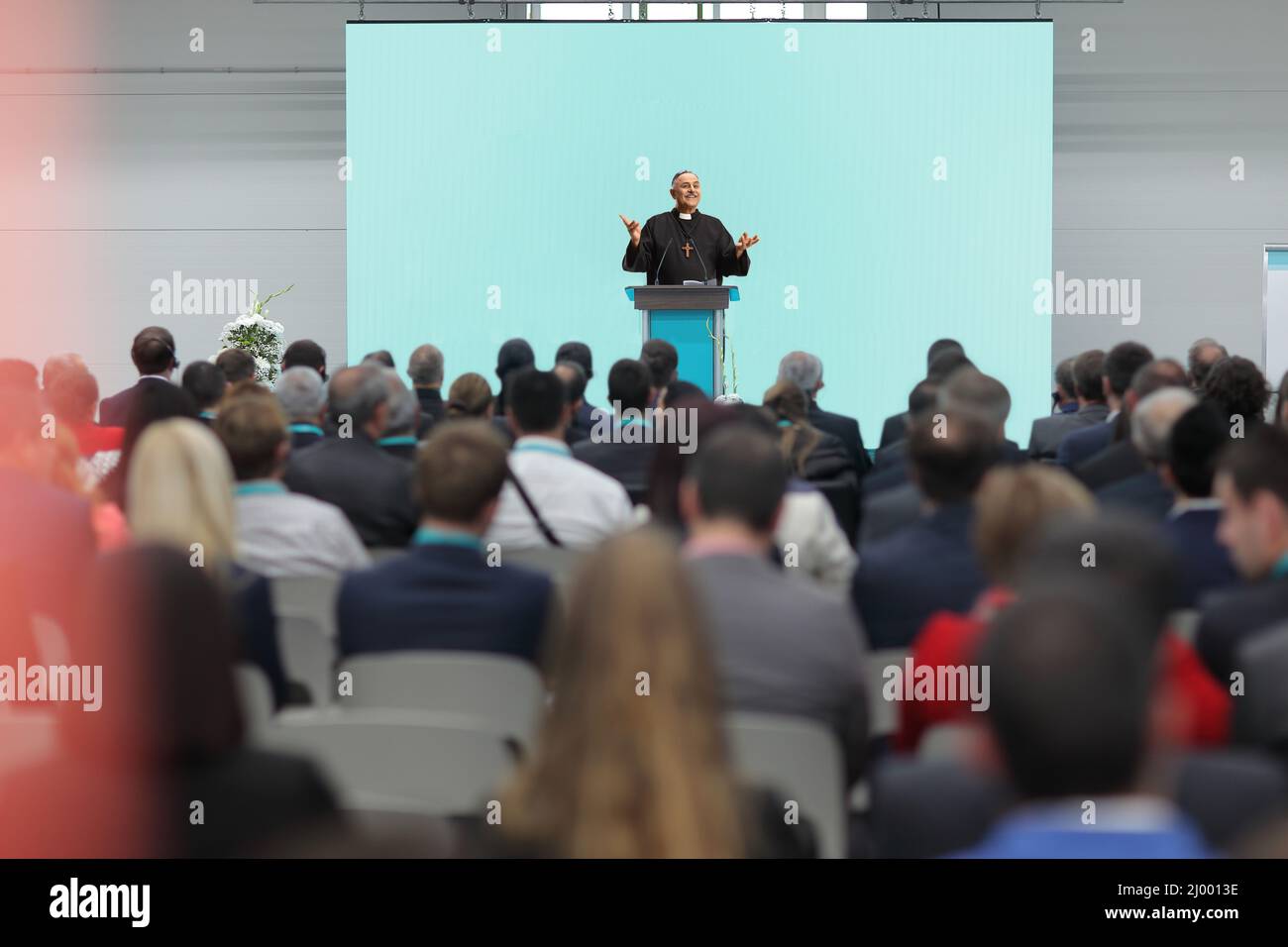 Priest talking on a speaker podium in front of audience inside a hall Stock Photo