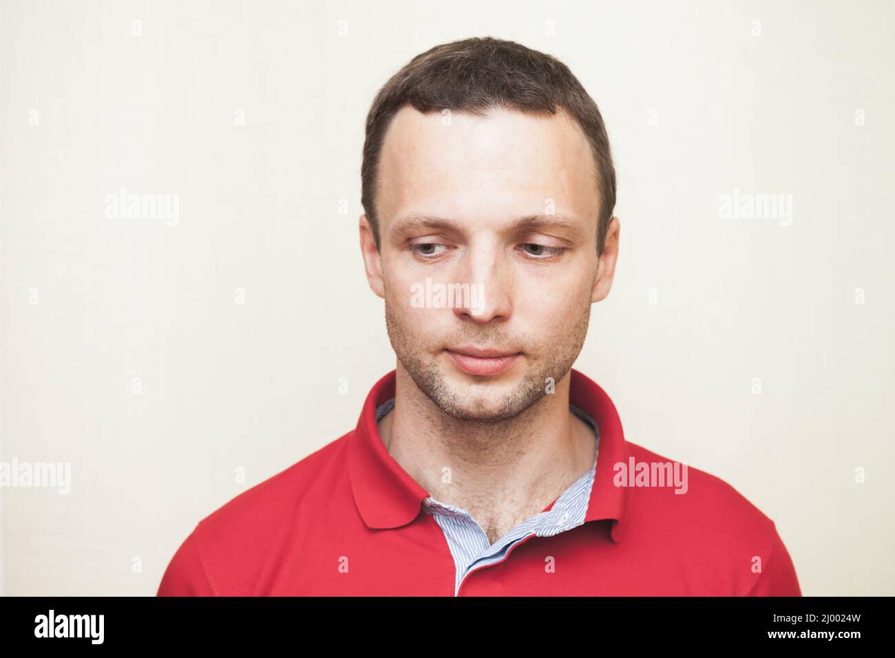 Close-up studio portrait of young adult European man in red polo shirt looking down Stock Photo