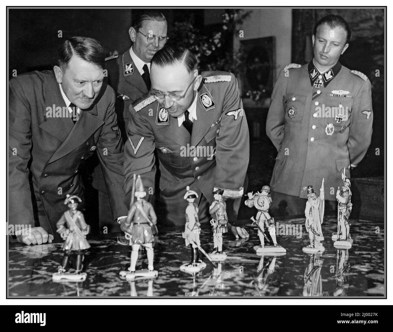 Adolf Hitler Fuhrer & Dictator of Nazi Germany and Heinrich Luitpold Himmler Reichsführer of the Schutzstaffel (Protection Squadron; SS), and a leading member of the Nazi Party (NSDAP) of Germany admire a collection of porcelain figures which have been made in detailed historic soldiers uniforms. Heinrich Hoffmann’s photograph in Obersalzberg on April 20, 1944, which Heinrich Himmler presents these Allach porcelain figures to Adolf Hitler for his 55th birthday. Allach porcelain Porzellan Manufaktur Allach was produced in Germany between 1935 and 1945. by forced Dachau concentration camp labour Stock Photo