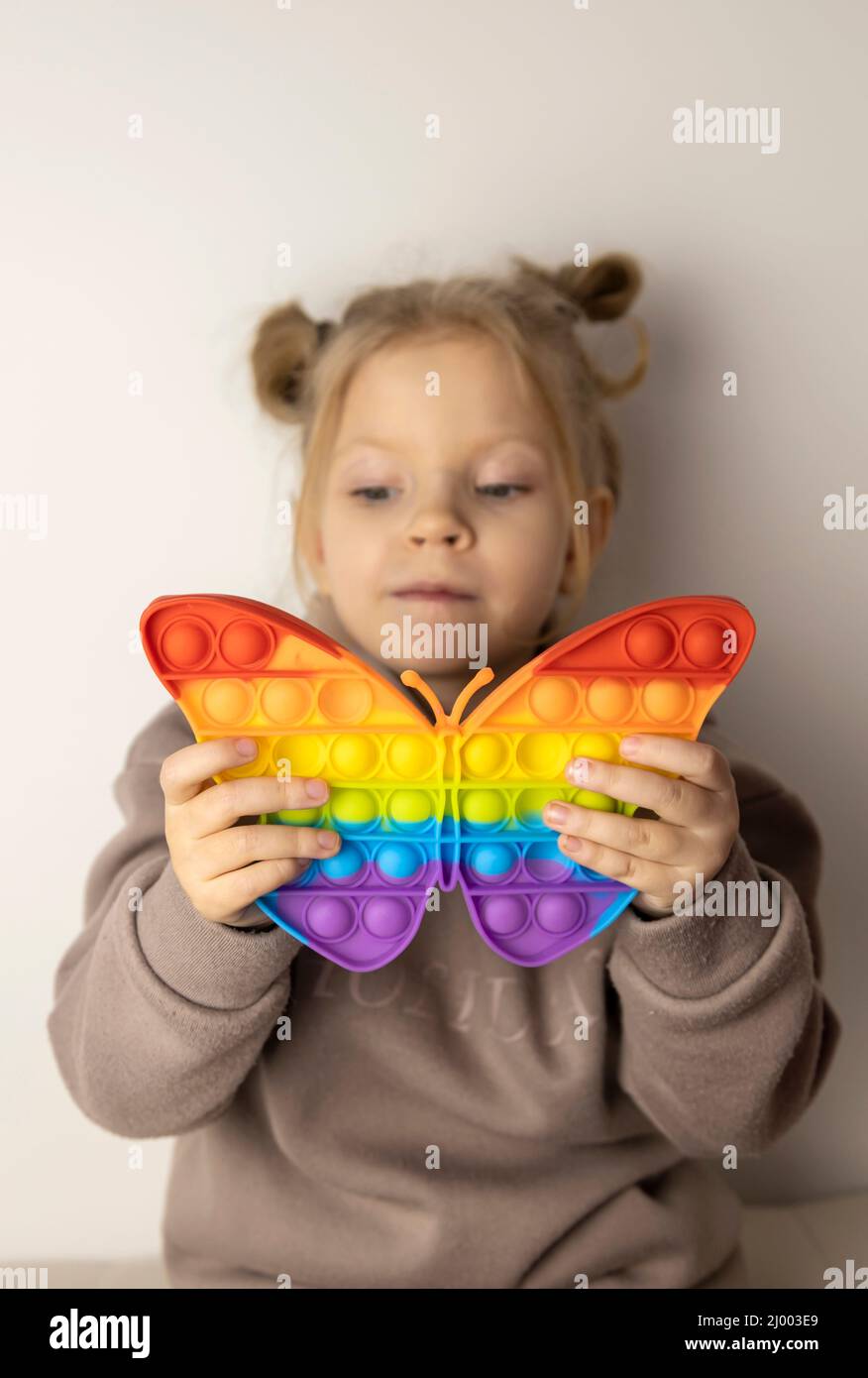 A 5-year-old girl plays with a Pop It toy in the shape of a butterfly. Popular anti-stress toy that develops fine motor skills. Focus on toys. Stock Photo