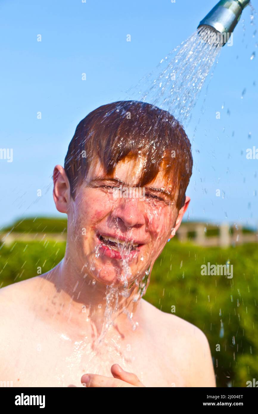 boy has a shower at the beach after swimming in the ocean Stock Photo