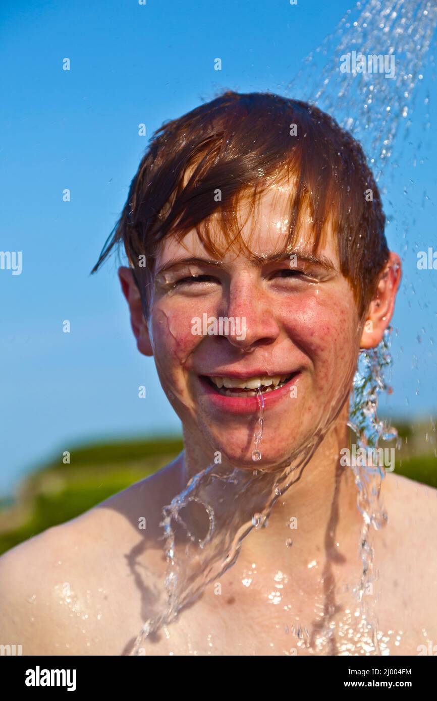 boy has a shower at the beach after swimming in the ocean Stock Photo