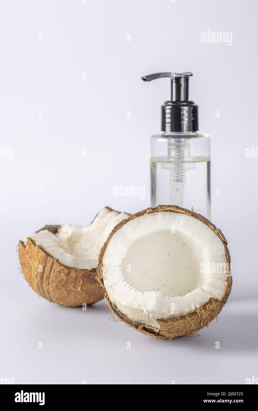 Coconut oil in a transparent bottle and fresh coconut on a white background. Natural cosmetic product for face, body and hair. Vertical format Stock Photo