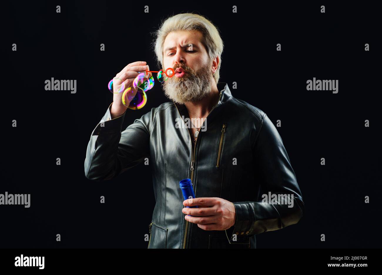 Handsome man blowing bubbles. Play with Soap bubble. Bearded guy in leather jacket. Good mood. Stock Photo