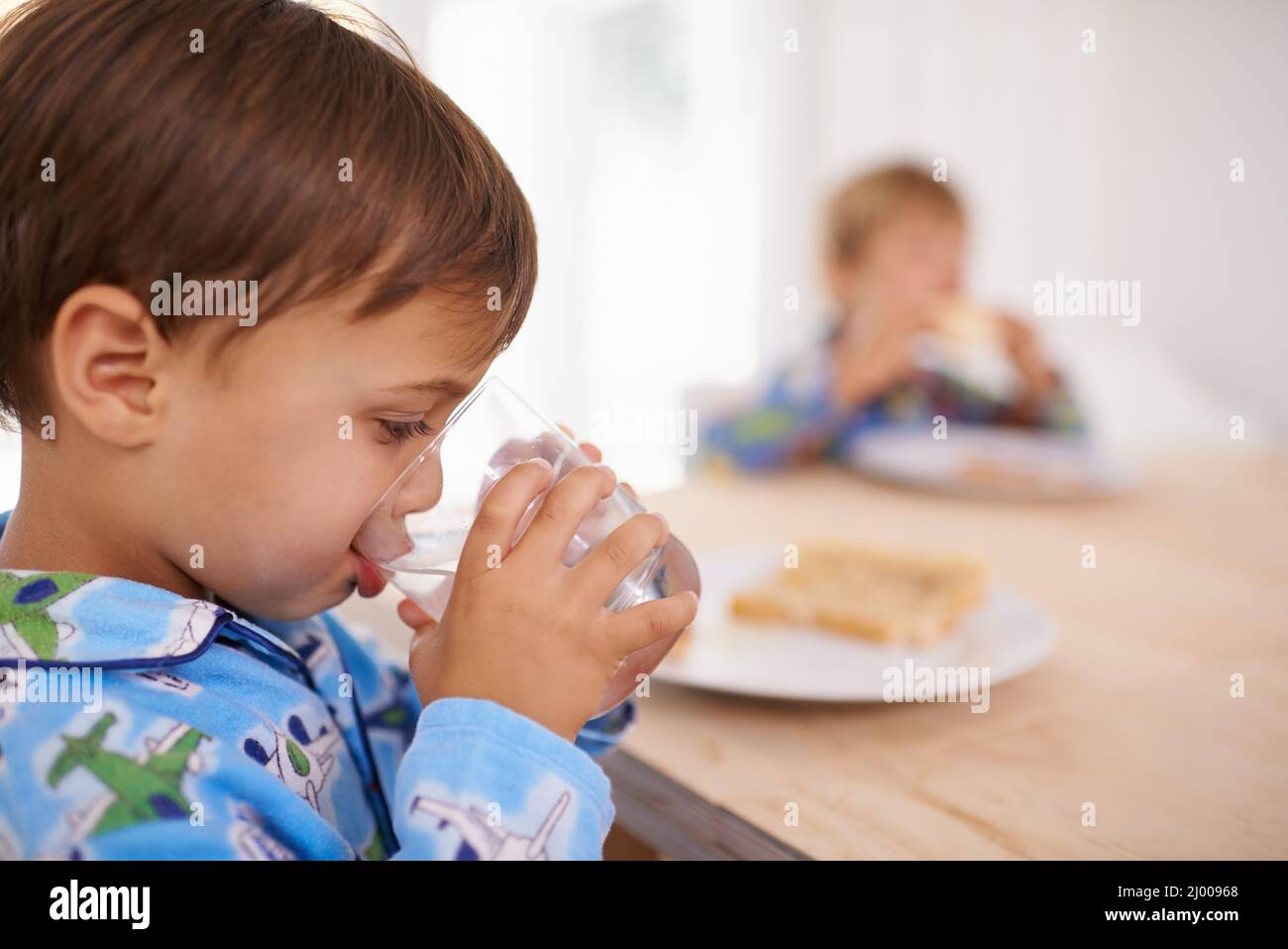 Washing it down. A cute little boy having a drink of water with breakfast. Stock Photo