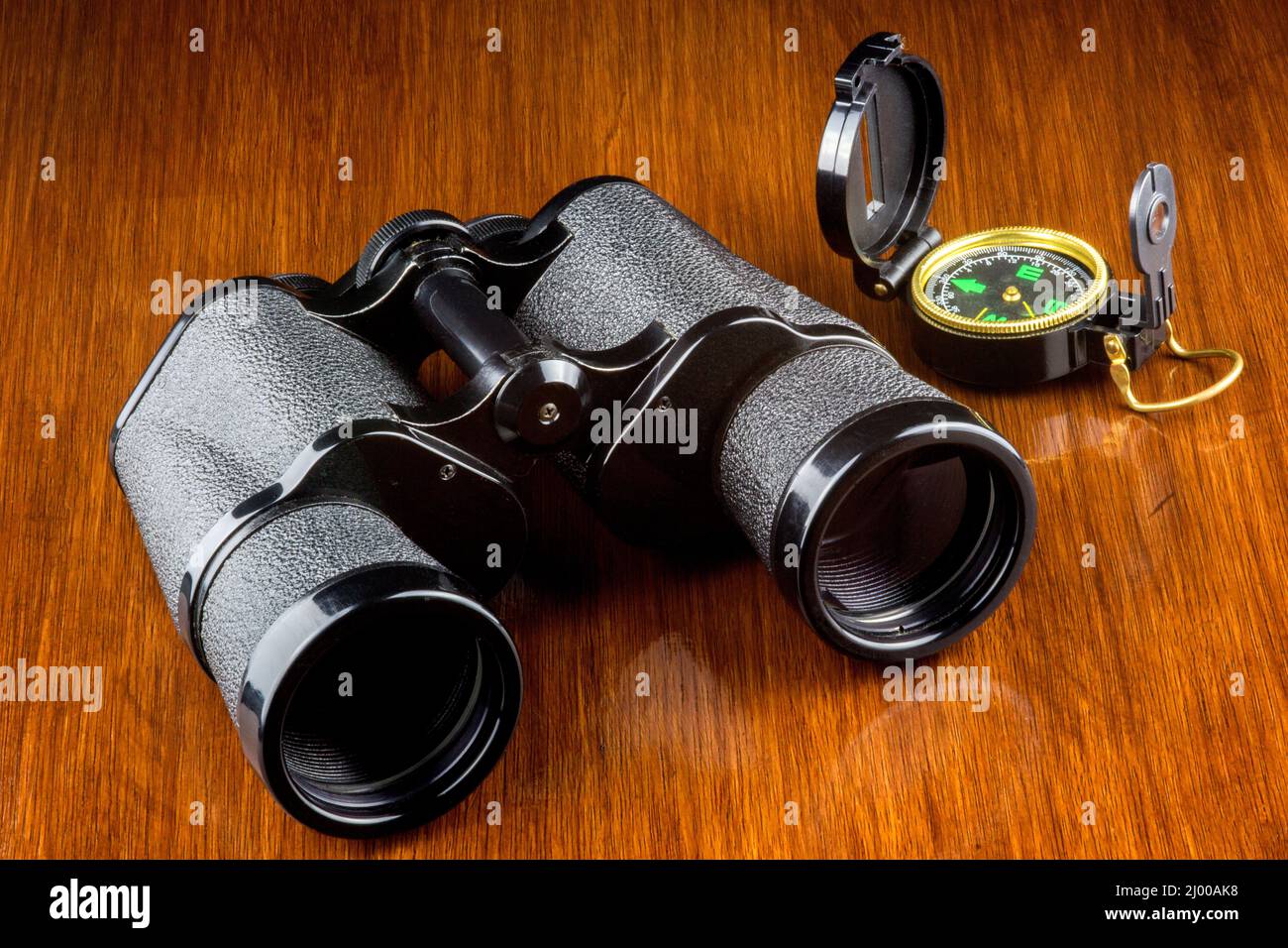 Binoculars and compass on a varnished wooden surface Stock Photo