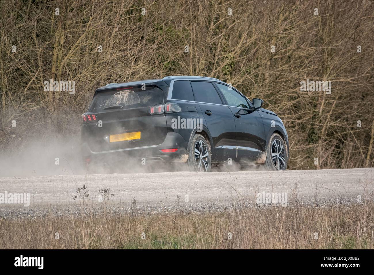 Black Peugeot 5008 GT sport utility vehicle driving along an unmade stone track road thowing up dust Stock Photo