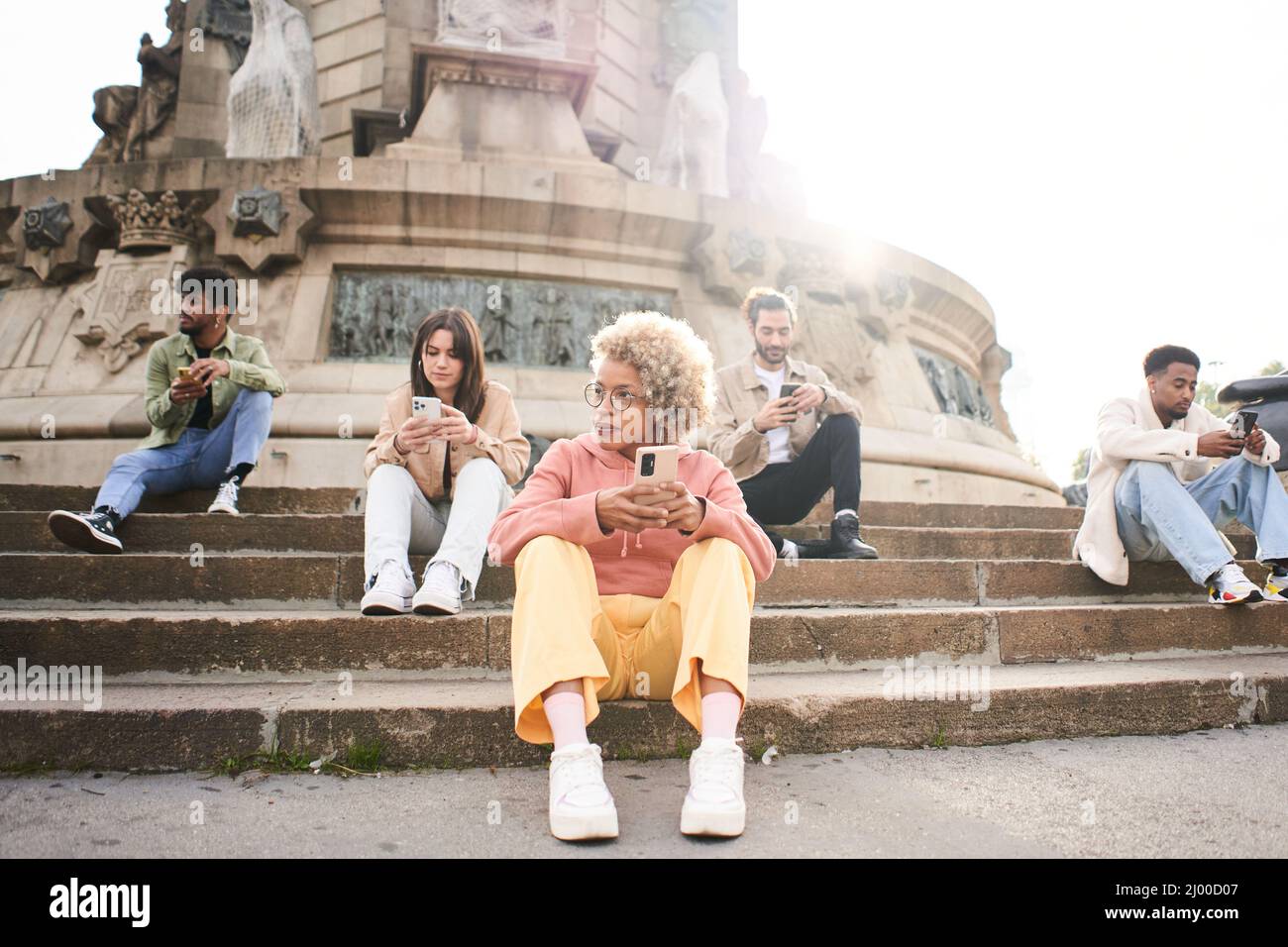 Group of people using phone with serious face. Friends focused on their mobiles sitting on a staircase in a city and a woman looks to the side Stock Photo