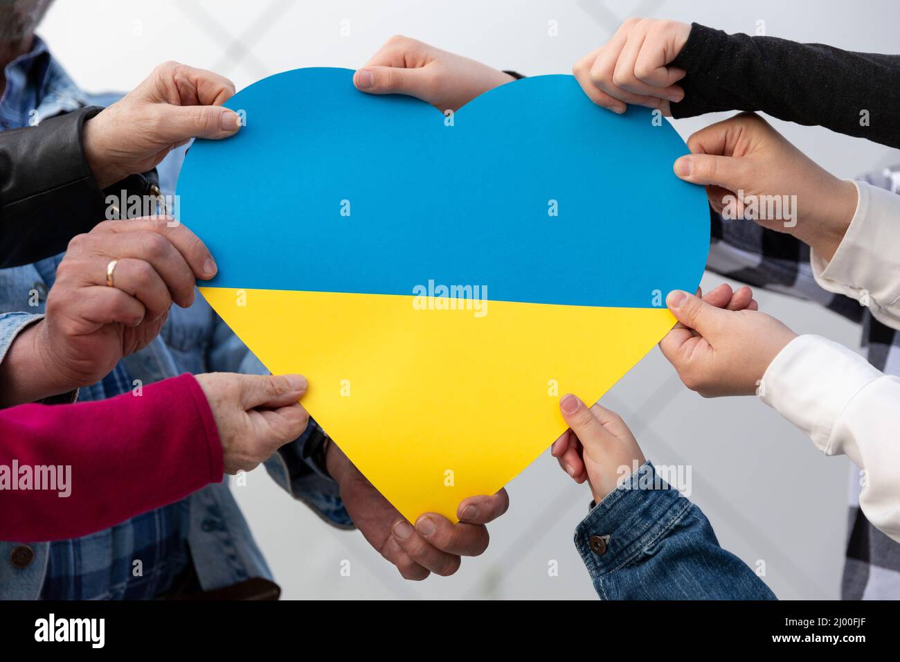 Many hands of different people holding a big heart with colors of Ukrainian flag. Freedom and support for Ukraine. Stop war. Stock Photo