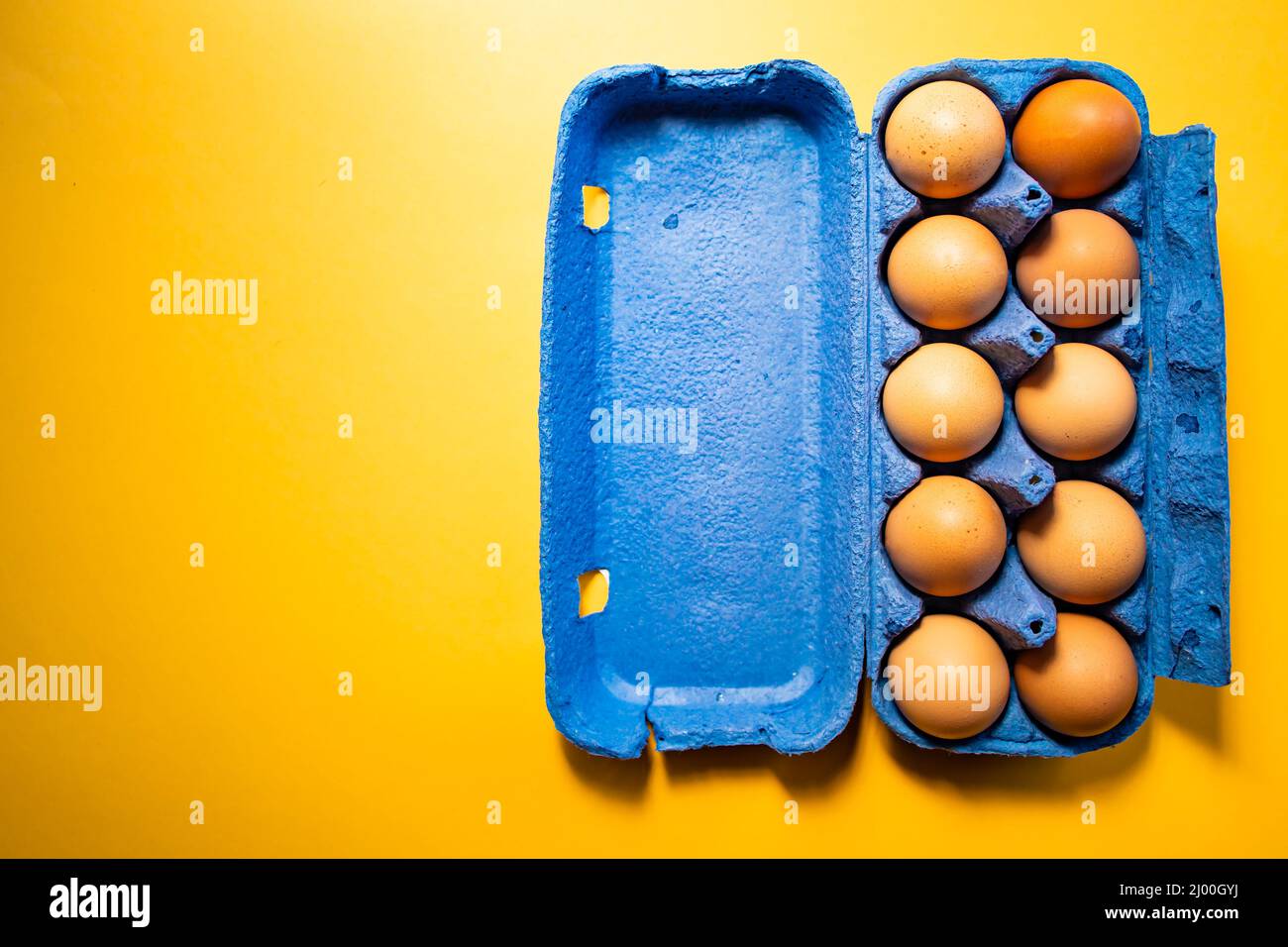 Blue eggs container with ten eggs, on yellow background. Copy space Stock Photo